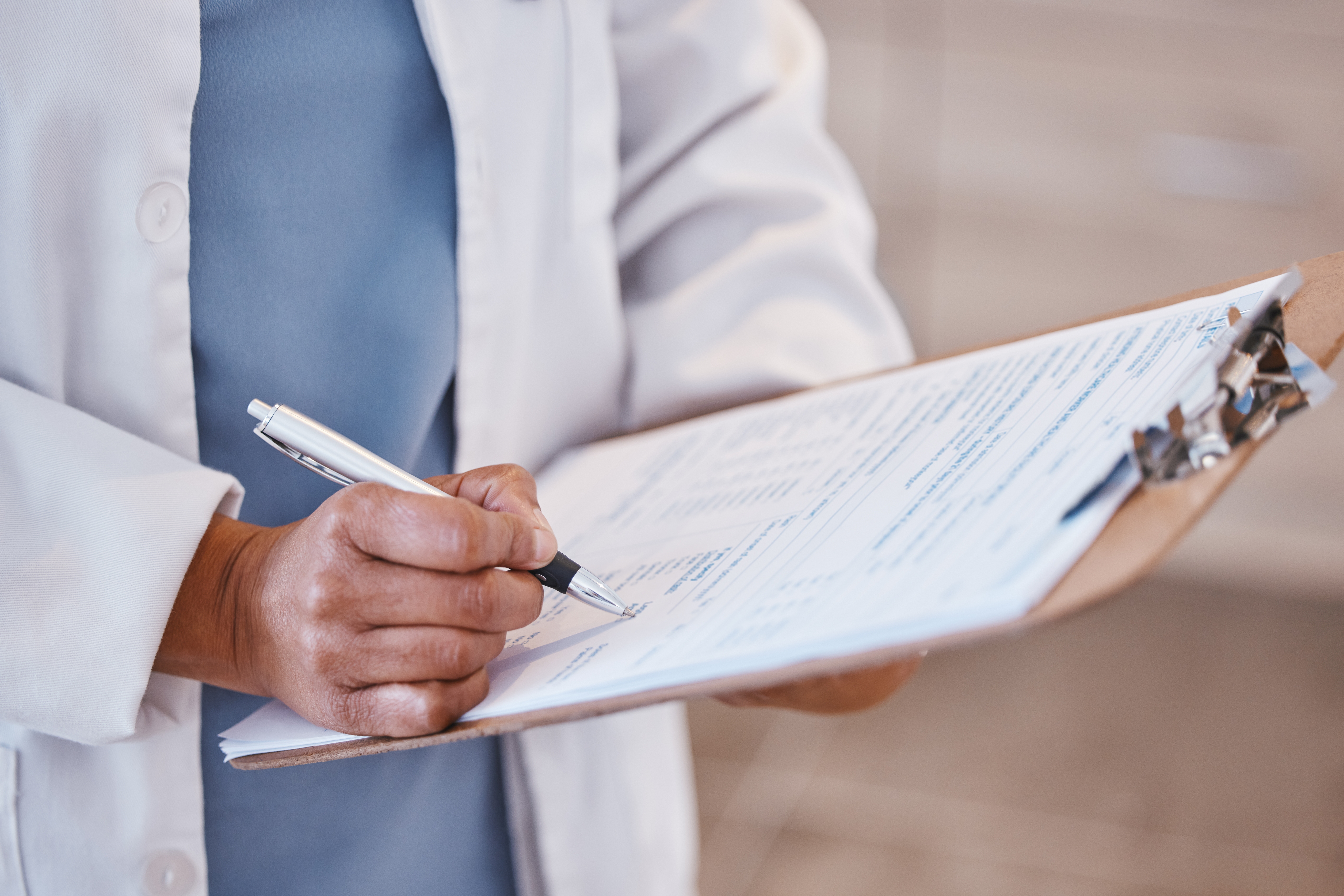 Healthcare worker in a white coat filling in a paper form on a clipboard